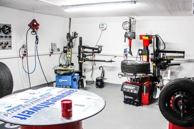 Das Bild zeigt eine helle Werkstatt mit FASEP-Reifenmontiermaschine, Auswuchtgerät, montierten Reifen, Druckluftanschlüssen und Rundtisch mit Divinol-Aufdruck im Vordergrund.