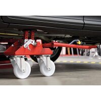 Das Bild zeigt einen roten hydraulischen Wagenheber auf vier weißen Lenkrollen, der unter einem Auto platziert ist, um das Fahrzeug für Reparatur- oder Rangierarbeiten anzuheben; der Wagenheber ist mit Metallteilen, Hebeln und einem Griff ausgestattet und steht auf einem glatten Werkstattboden.