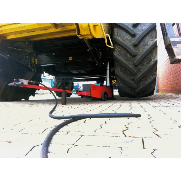 Das Bild zeigt einen roten, mobilen hydraulischen Wagenheber mit zwei großen Gummirädern, einem langen senkrechten Griff und einem ausfahrbaren, silbernen Hubzylinder. Das Gerät ist für das Anheben schwerer Lasten wie zum Beispiel Fahrzeuge geeignet und steht auf einer flachen, schwarzen Grundplatte.