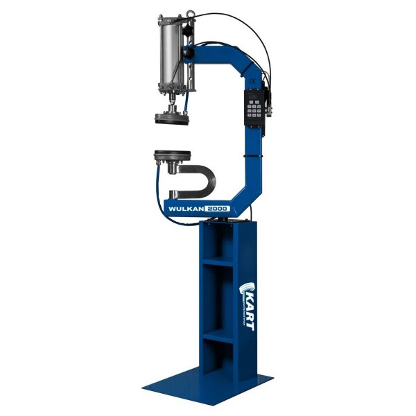 Das Bild zeigt eine große, freistehende blaue Industriemaschine mit rechteckigem Standfuß und offenem Rahmen. Im oberen Bereich befindet sich ein silberner, zylindrischer Mechanismus mit Schläuchen und einer Steuerungseinheit mit Tastenfeld rechts am Rahmen. Zwei runde Metallscheiben sind versetzt übereinander angebracht. Auf dem Rahmen steht in weißer Schrift „WULKAN 2000“ und am Standfuß ist das weiße Logo „KART“ angebracht. Die Maschine wirkt funktional und robust.