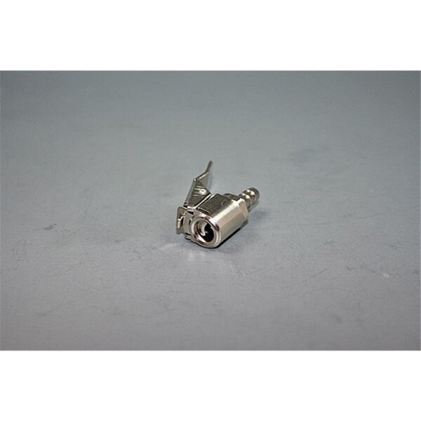 Das Bild zeigt einen kleinen, metallenen Steckverbinder oder Adapter, der auf einer grauen Oberfläche liegt. Der Adapter hat einen zylindrischen Körper mit einer Öffnung an einem Ende und einem Hebelmechanismus an der Seite. Die Oberfläche ist glatt, und das Metall glänzt im Licht. Der Hintergrund ist einfach und einfarbig, sodass der Fokus auf dem Adapter liegt.