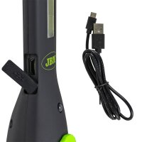Das Bild zeigt den unteren Teil eines schwarzen Geräts mit grünen Akzenten und dem Schriftzug JBM in grün, an dessen Seite eine Gummiabdeckung mit USB-Symbol geöffnet ist und einen USB-Anschluss freilegt; daneben liegt ein schwarzes Kabel mit einem USB- und einem Micro-USB-Stecker.