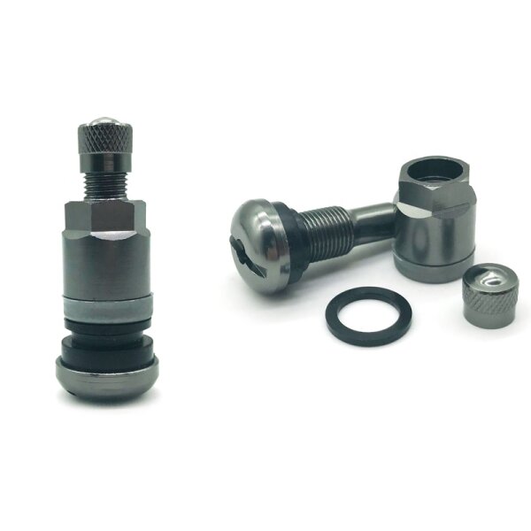Das Bild zeigt zwei metallische Autoventile mit Schraubgewinde, Dichtungsringen und abnehmbaren Verschlusskappen, daneben liegt zusätzlich eine schwarze Gummidichtung, alle Teile sind silberfarben und liegen auf weißem Hintergrund.