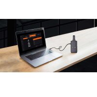 Ein silberner Laptop steht auf einem hellen Holztisch, sein Bildschirm zeigt eine Software zur Programmierung eines Funkgeräts an. Das Funkgerät liegt rechts daneben und ist mit einem Kabel über USB mit dem Laptop verbunden. Im Hintergrund sind dunkle Möbel erkennbar.