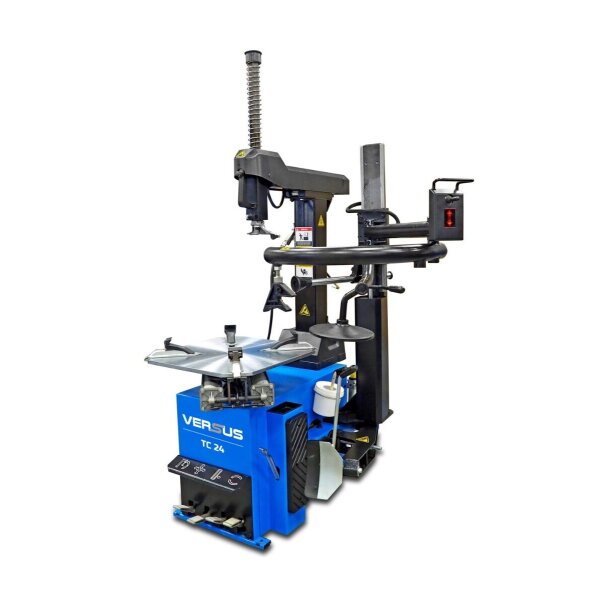 Das Bild zeigt eine blaue Reifenmontiermaschine mit der Aufschrift „VERSUS TC 24“. Die Maschine besteht aus einem rechteckigen Grundkörper mit verschiedenen Bedienelementen und einem großen metallenen Drehteller auf der Oberseite, auf dem Reifen montiert werden können. Seitlich ist ein schwarzer Arm mit zusätzlichen Werkzeugen und einem runden schwarzen Halter angebracht. Oben befindet sich eine schwarze Haltevorrichtung mit einem spiralförmigen Metallelement. Die Maschine steht vor weißem Hintergrund und wirkt robust und industriell.