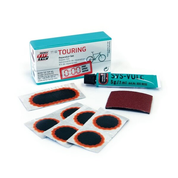 Das Bild zeigt ein Fahrrad-Flickzeug-Set mit einer hellgrünen Aufbewahrungsbox, mehreren runden und ovalen Flicken mit schwarzer und oranger Umrandung, einer Tube Vulkanisierlösung, einem kleinen Stück Schleifpapier und einem kurzen, hellen Kunststoffröhrchen.
