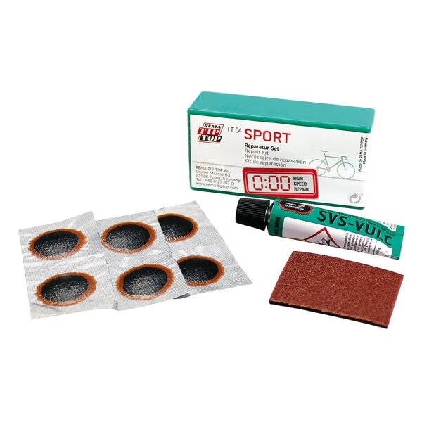 Das Bild zeigt ein Fahrrad-Flickzeug-Set bestehend aus einer grünen Schachtel mit der Aufschrift Sport Reparatur-Set, sechs runden selbstklebenden Flicken, einer kleinen Tube mit Vulkanisierflüssigkeit sowie einem rechteckigen Stück Sandpapier.