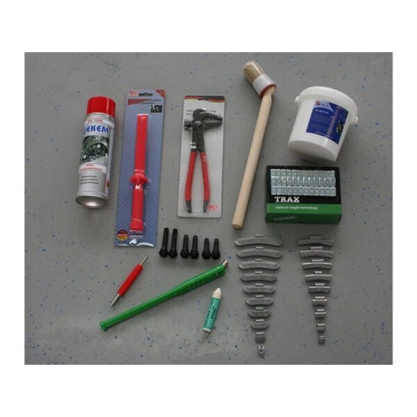 Das Bild zeigt verschiedene Werkzeuge und Materialien, die auf einer grauen, leicht gesprenkelten Fläche ausgebreitet sind: Eine Sprühdose, ein rotes Kunststoffwerkzeug, eine Zange mit rotem Griff in Blisterverpackung, ein runder Pinsel mit Holzstiel, ein weißer Eimer mit blauem Etikett, eine grüne Schachtel mit kleinen Metallgewichten, vier schwarze Gummiventile, acht silberne Reifenwuchtgewichte in zwei Reihen, ein roter Handgriff mit Metallspitze, ein langer grüner Stift ähnlich einem Schraubendreher und eine kleine grüne Kreide.